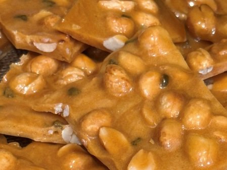 8976b480-cc1a-4fa3-b246-d2cbbc1686c8 Close-up image of peanut brittle pieces, showcasing a rich golden color with visible peanuts embedded in a crunchy, caramelized texture. Ideal for dessert lovers and snack enthusiasts.