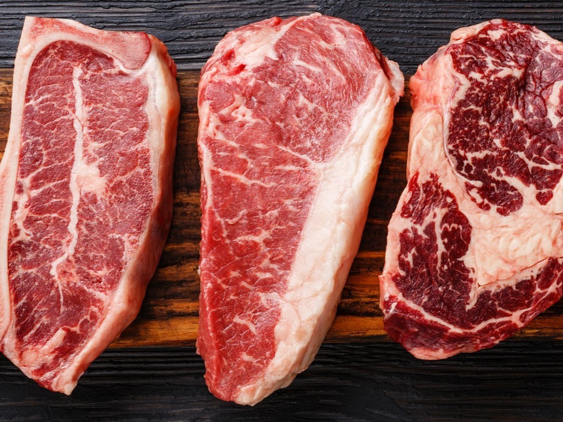 beef_nystrip Three cuts of premium beef steaks displayed on a wooden cutting board, showcasing marbling and texture, ideal for grilling or roasting.